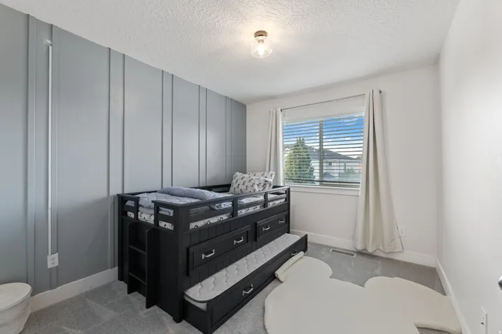 Textured accent wall, window with blinds, overhead light fixture, light gray carpeting, white trim