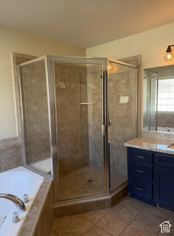 Tiled shower enclosure with a glass door, corner soaking tub with chrome fixtures, and a vanity with granite-style countertop and blue cabinetry