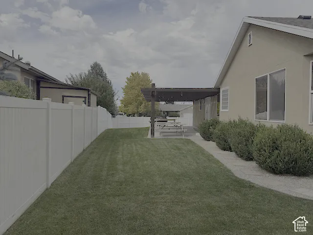 Expansive lawn area with a white privacy fence and a paved patio featuring a pergola