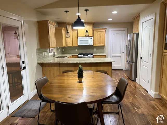Wood-finish flooring with light wood cabinetry, a tiled backsplash, and stainless steel appliances