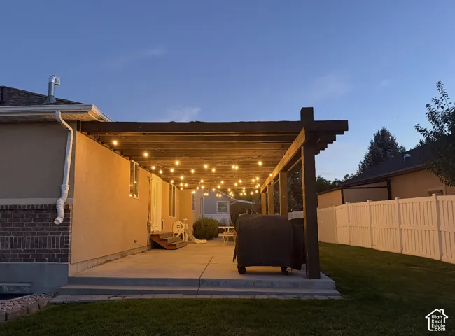 Expansive concrete patio with a dark wood pergola, string lighting, and stucco exterior