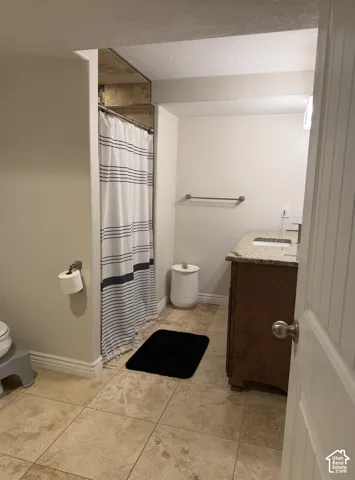 Tiled flooring, built-in vanity with stone countertop, shower with textured wall panels, wall-mounted towel bar