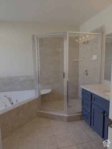 Spacious bathroom featuring a corner shower enclosure, built-in bathtub, blue vanity with countertop, and ceramic tile flooring