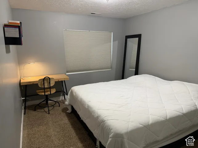 Window with blinds, wall-mounted shelving unit, wood-finish desk, and carpeting