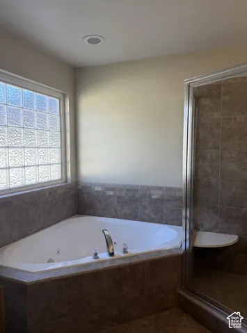 Corner jetted tub with tile surround, glass block window, and adjacent glass-enclosed shower with built-in bench