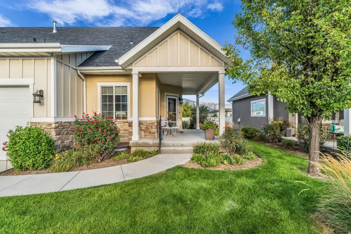 Covered porch entry, stone facade accents, vertical board siding, concrete walkway, and manicured landscaping