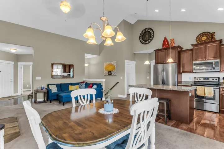 Open-concept living area with vaulted ceilings, a kitchen island, stainless steel appliances, and wood-finish flooring