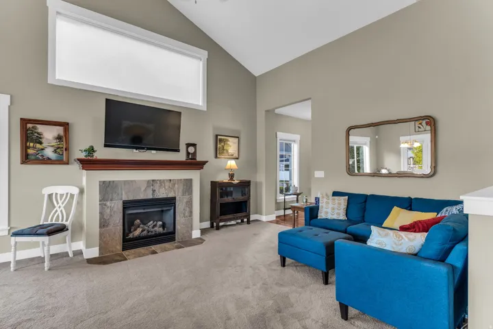 Vaulted ceiling, stone surround fireplace with wood mantel, upper transom window, and carpet flooring