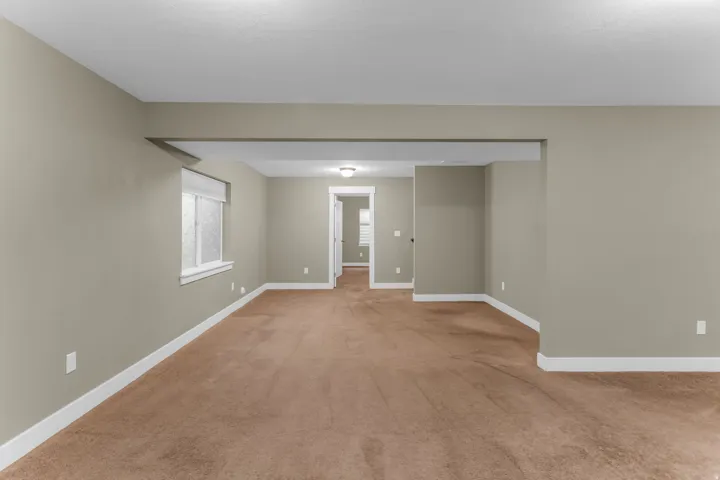 Expansive room featuring neutral wall tones, brown carpet flooring, and a single window with a privacy blind