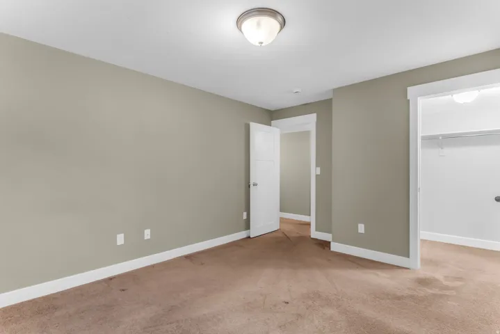 Neutral tone wall color, brown carpeting, white trim, recessed lighting, and a closet with shelving and hanging rod
