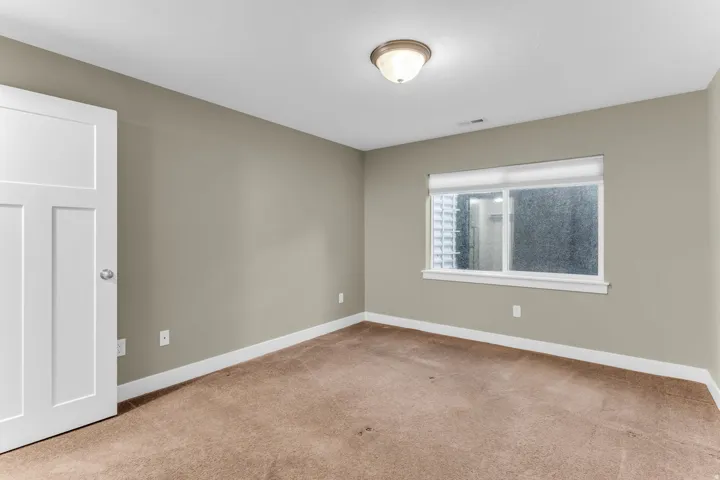 Neutral paint tones, white trim, recessed window, flush-mount ceiling light, and carpeted flooring