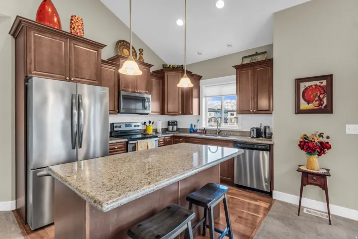 Kitchen featuring wood-finish flooring, stainless steel appliances, a large center island with a stone countertop, a tile backsplash, and recessed lighting