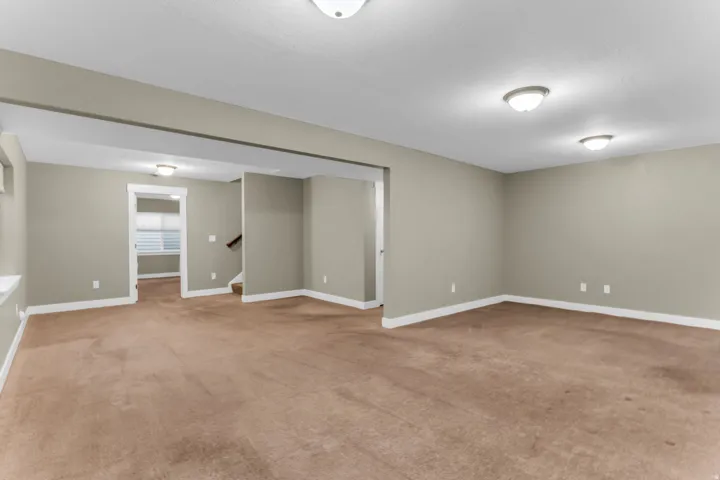 Recessed ceiling lights illuminate a spacious room featuring neutral-toned walls, brown carpeting, and white baseboards