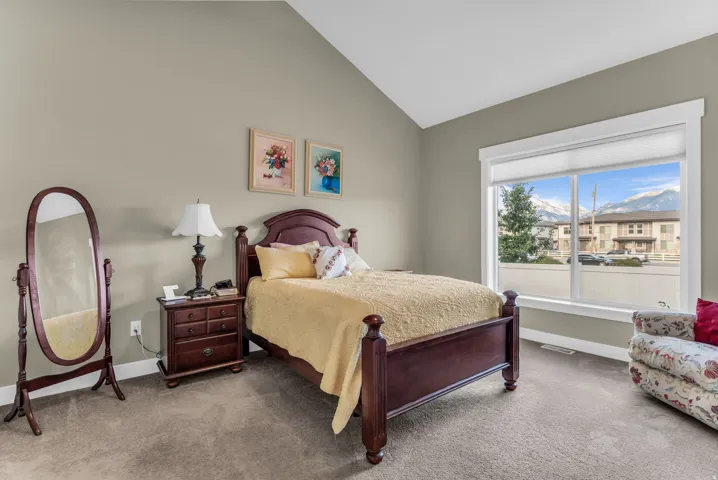 Vaulted ceiling, neutral wall paint, large picture window, mountain scenery, and carpet flooring