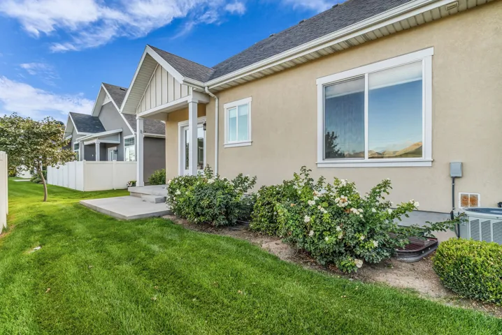 Back patio, expansive green lawn, mature landscaping, concrete patio, stucco exterior, and white vinyl fencing