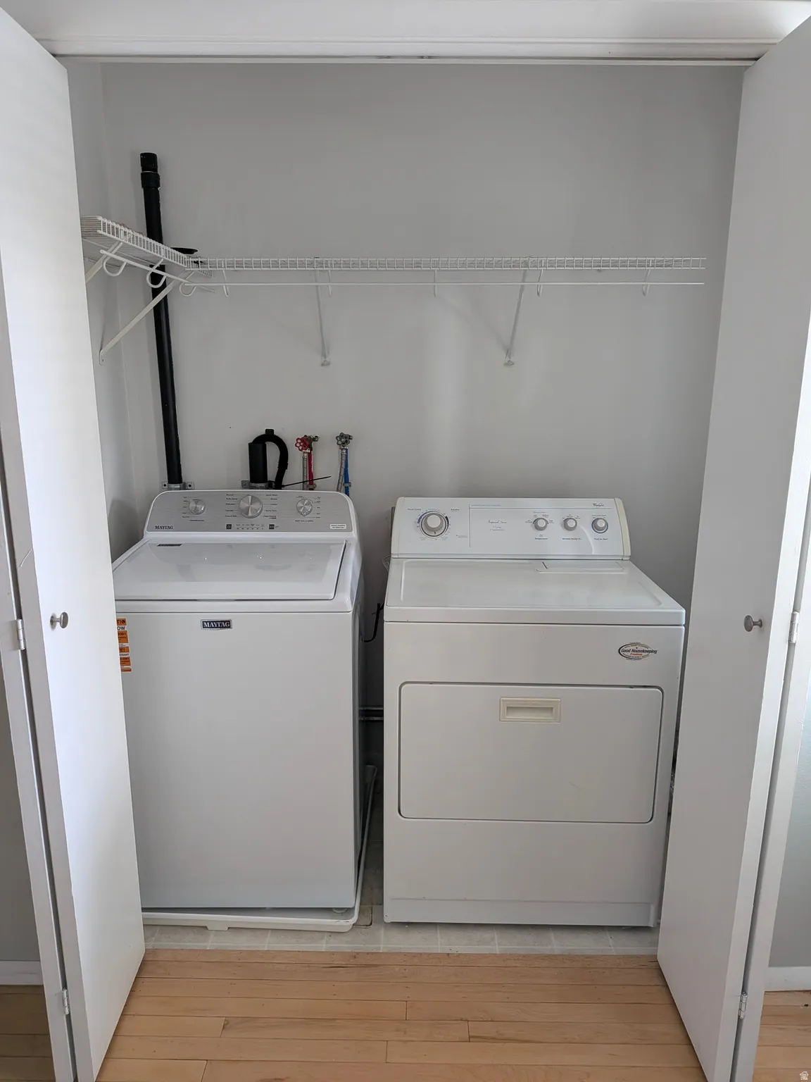 Enclosed laundry area featuring a top-load washing machine, front-load dryer, and wall-mounted wire shelving