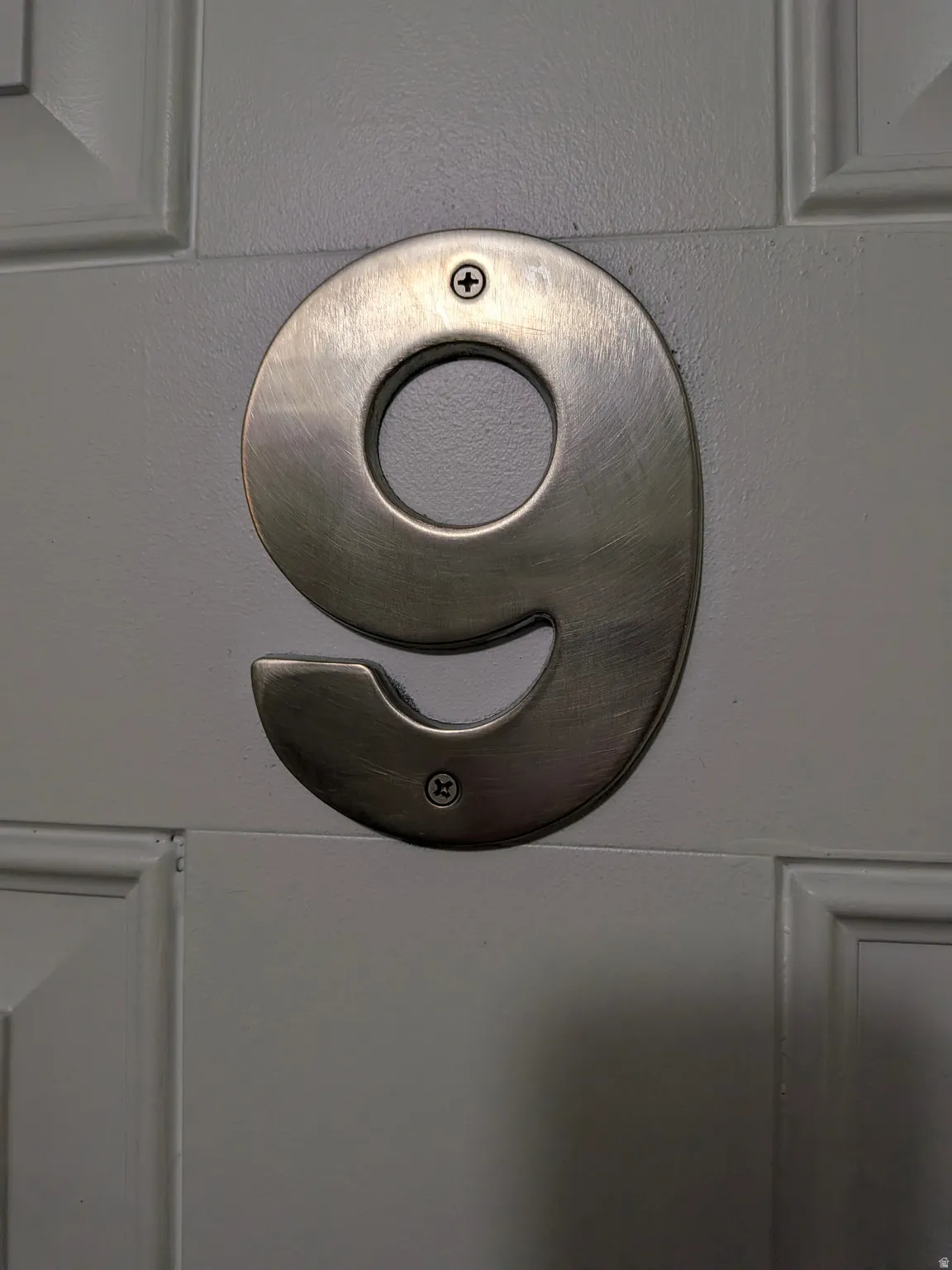 Brushed metal door numbering on a paneled door
