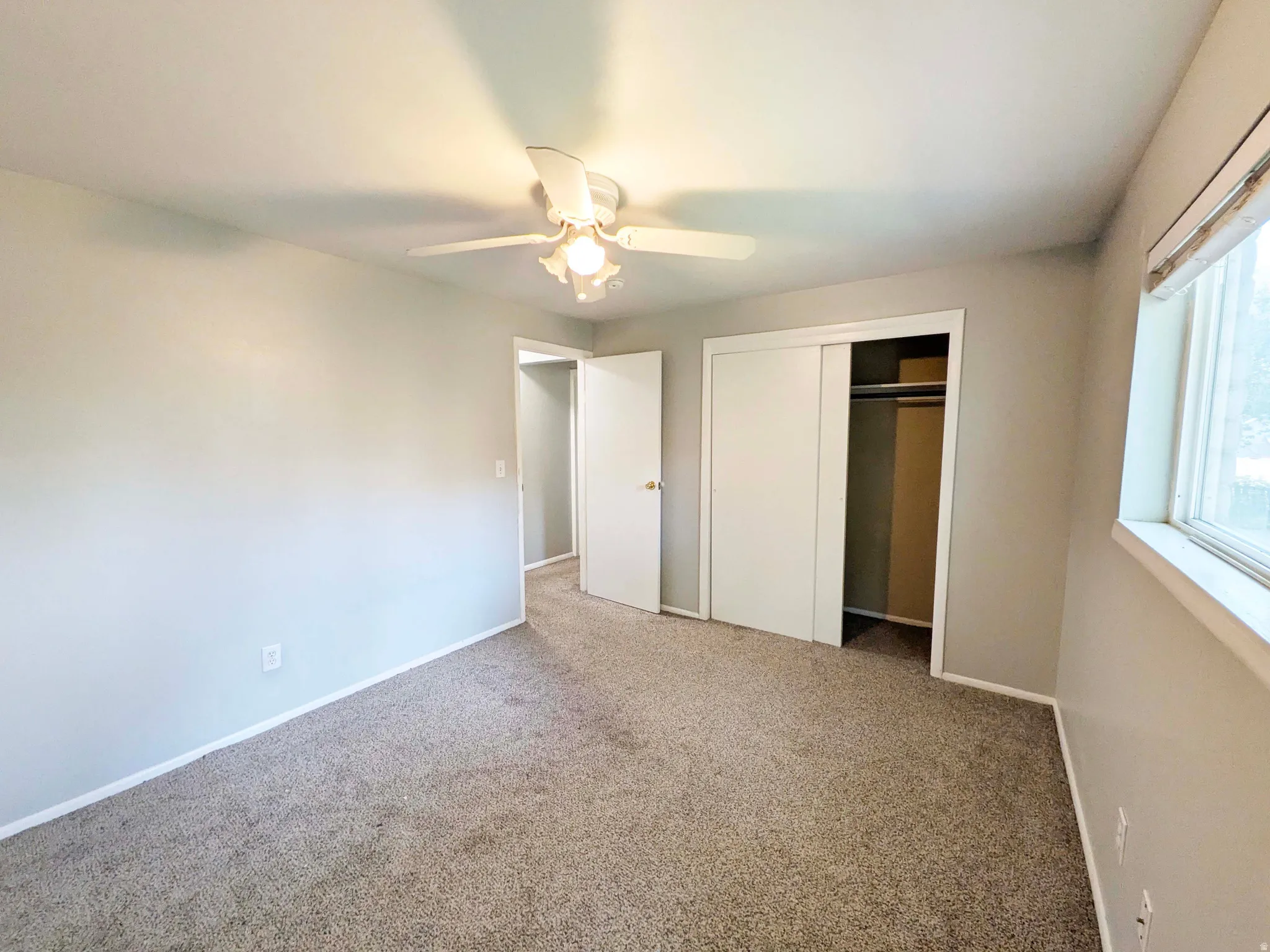 Carpeted room featuring a ceiling fan with integrated lighting, a window, and two closet areas