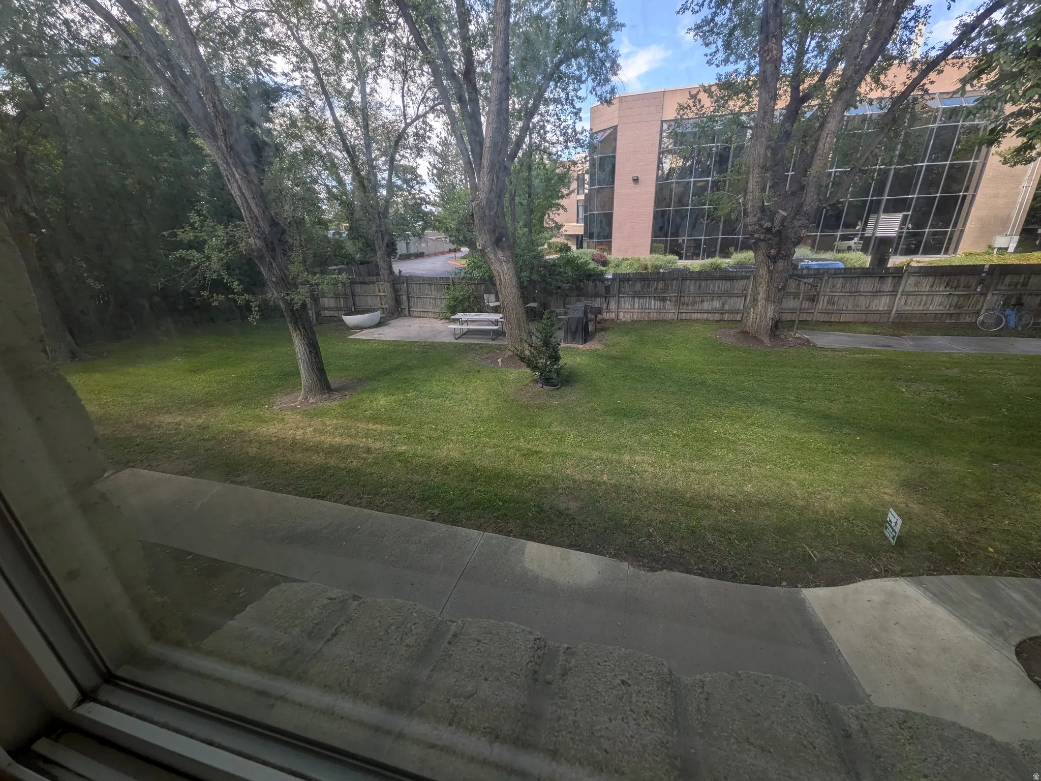 Expansive green lawn with mature trees, a private fenced area, and a paved patio space