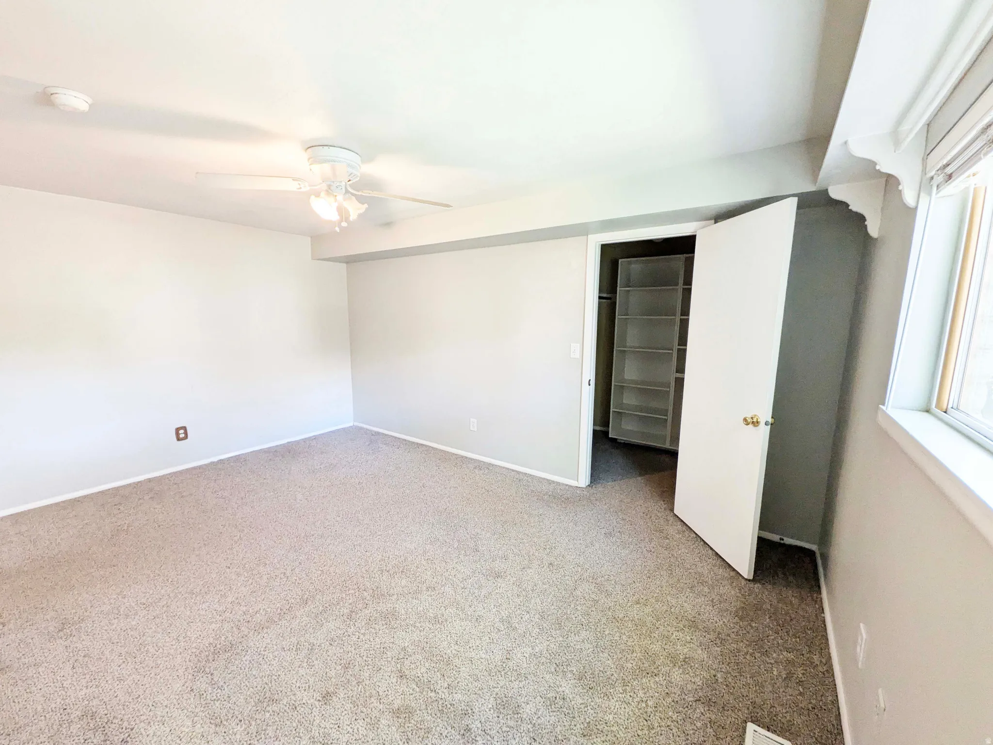 Plush carpeted flooring with a built-in closet featuring shelving, overhead lighting, and a ceiling fan
