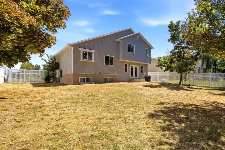 Rear exterior featuring gray siding, white trim, multiple windows, and a white fence enclosing the yard