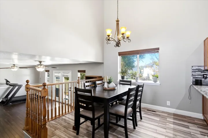 Open-concept dining and kitchen area featuring a black dining table with seating for four, wood-finish flooring throughout, pendant lighting fixture, stainless steel appliances, and abundant natural light from a large picture window