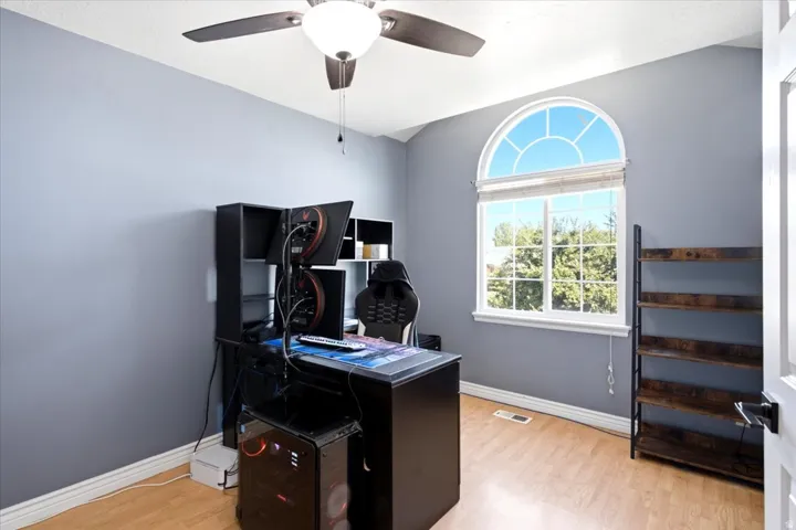 Modern home office featuring light wood-finish flooring, soft gray wall finishes, and abundant natural light from an arched transom window