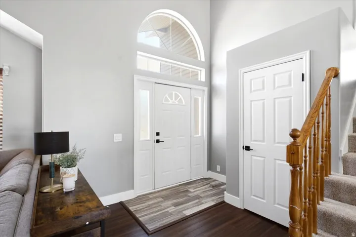 Two-story foyer featuring an arched transom window and sidelights, a paneled entry door, wood-finish flooring, and a carpeted staircase with wood banister