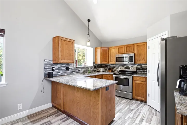 Kitchen featuring vaulted ceiling, wood-finish cabinetry, stainless steel appliances, mosaic tile backsplash, and light-toned countertops