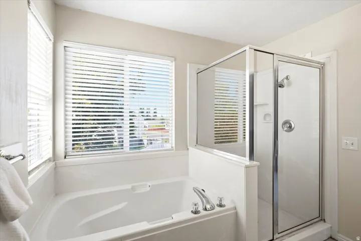 Alcove tub with chrome fixtures, an adjacent glass-enclosed shower, and a large window with white blinds