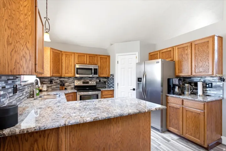 Kitchen featuring wood cabinetry, stainless steel appliances, a tile backsplash, and stone-finish countertops