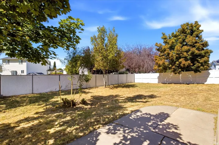 Spacious backyard with mature shade trees, concrete patio, and open lawn area bordered by perimeter fencing