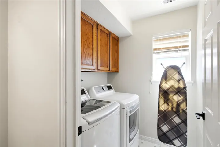 Utility room with wood-finish cabinetry, a window with blinds, and light-toned walls