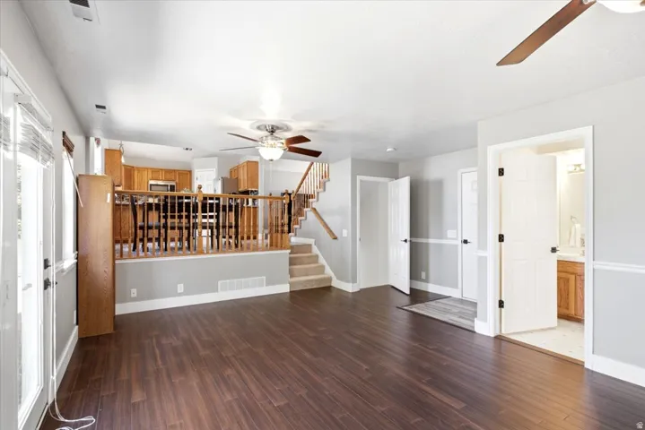 Open-concept living space with rich wood-finish flooring throughout, custom wooden railing detail, and abundant natural light from multiple windows