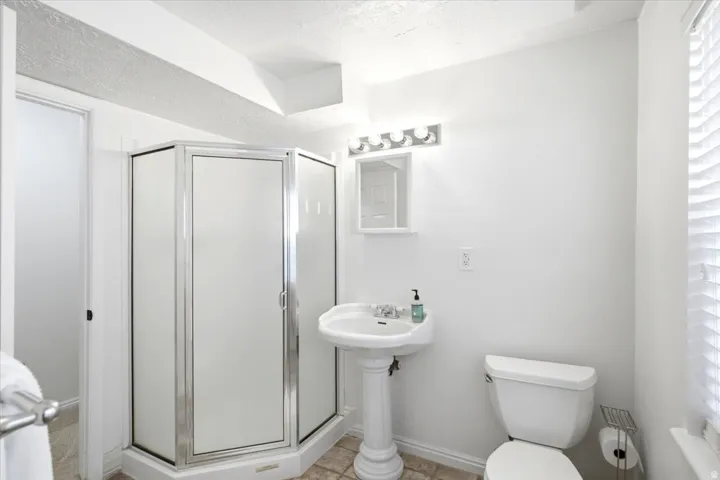 Pedestal sink with chrome faucet, shower enclosure with frosted panels, toilet, and window with blinds