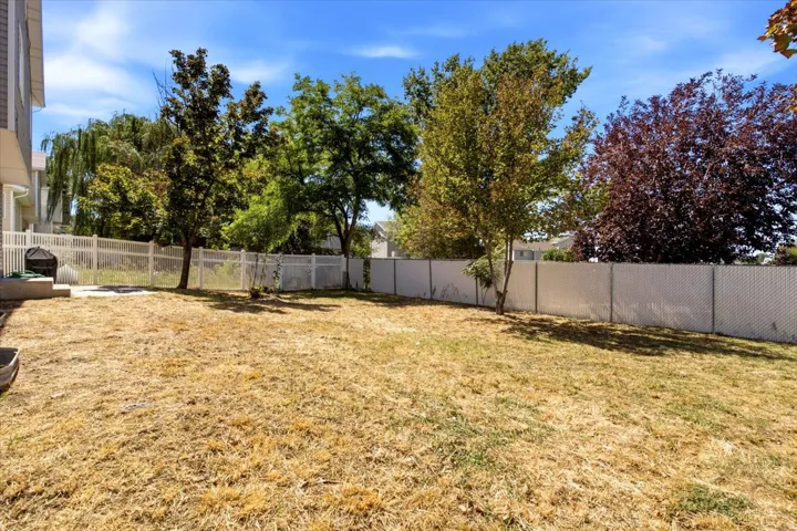 Fenced backyard featuring mature trees, a concrete patio, and a side exterior of the residence