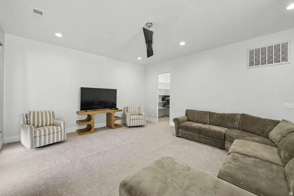 Recessed ceiling lighting, ceiling-mounted fan, light-toned carpeting, and a built-in shelving system