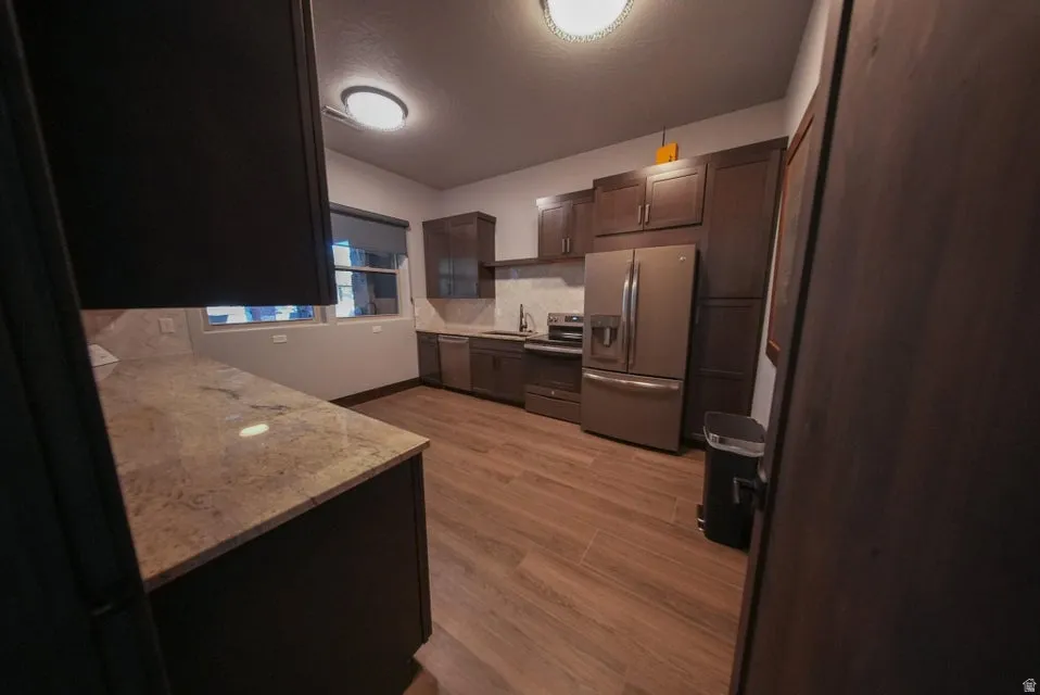Kitchen featuring wood-finish flooring, dark wood cabinetry, light-toned countertops, and stainless steel appliances