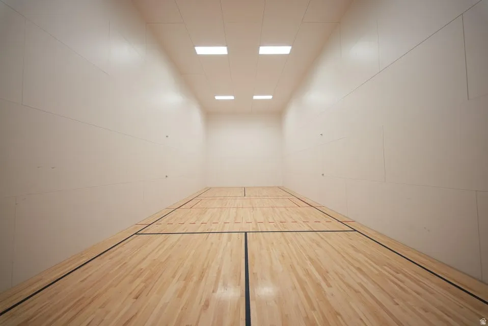 Indoor court featuring wood flooring with black and red court lines, white wall panels, and recessed ceiling lighting
