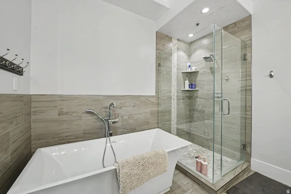 Freestanding soaking tub, glass-enclosed shower, integrated shower shelving, tile walls, and recessed lighting