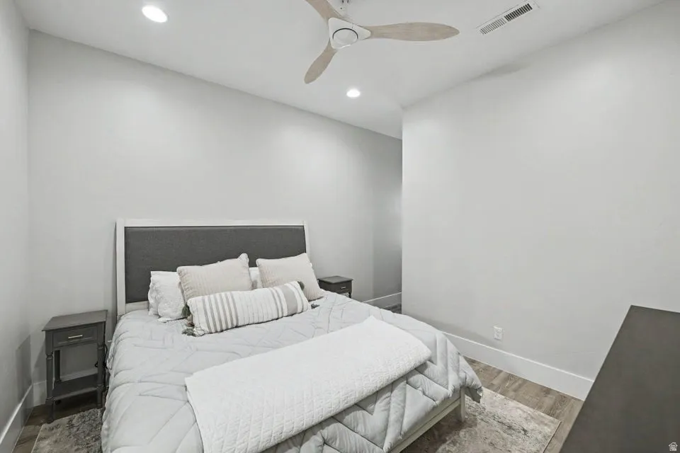 Modern secondary bedroom featuring a platform bed with upholstered headboard, recessed ceiling lighting, ceiling fan with brushed nickel finish, and neutral wall finishes