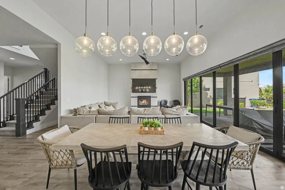 Vaulted ceiling with linear pendant lighting, fireplace with integrated media space, full-height sliding glass doors, and wood-finish flooring