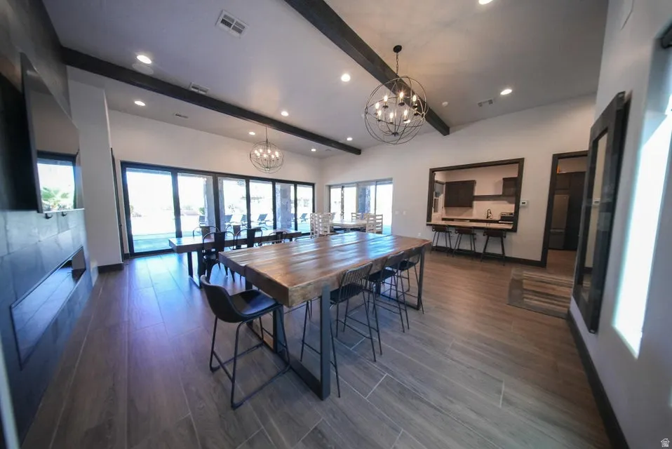 Vaulted ceiling with exposed wood beams, large format tile flooring, built-in linear fireplace, recessed lighting, and multiple spherical chandeliers