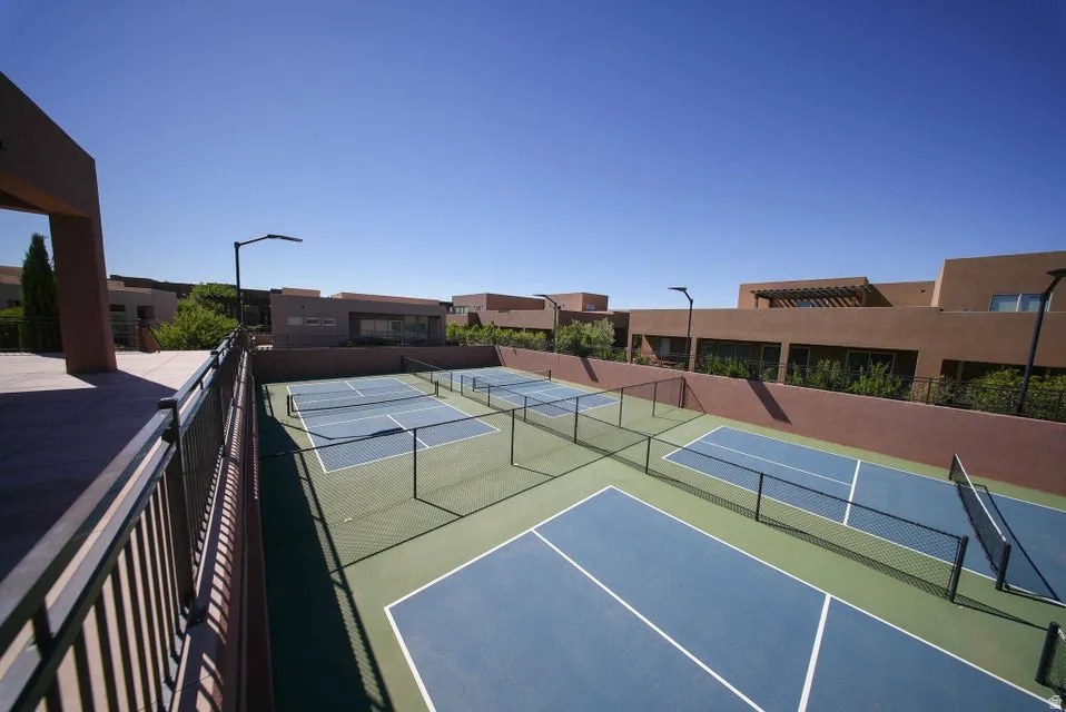 Multiple outdoor courts featuring blue playing surfaces, green surrounds, black fencing, and integrated lighting