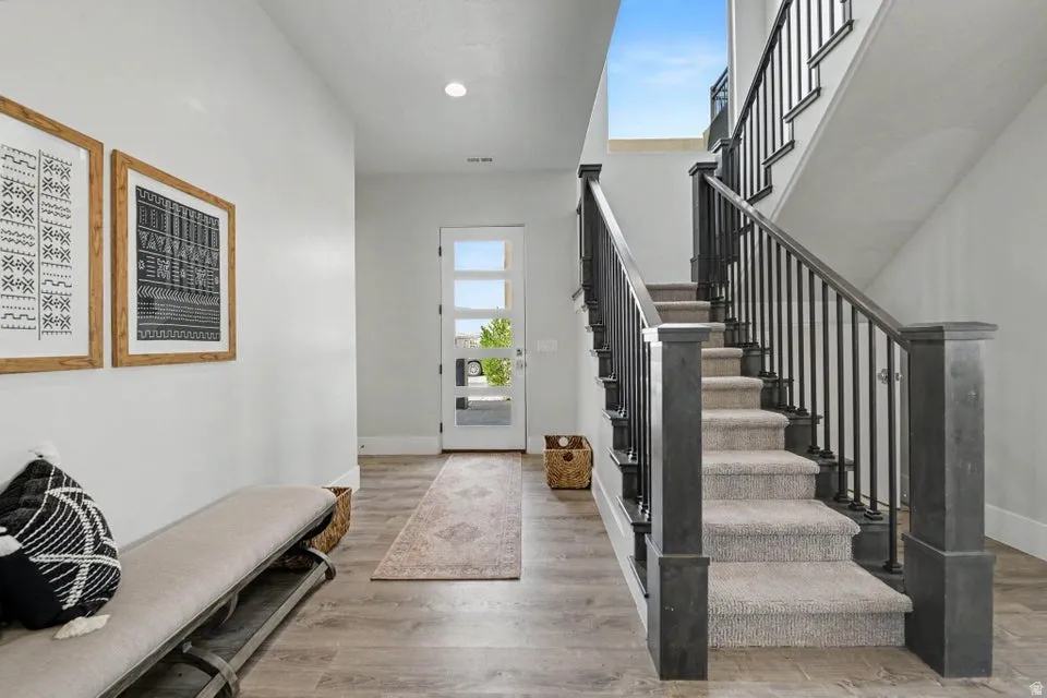 Bright foyer with soaring vaulted ceilings and skylights, wood-finish flooring, and a dramatic staircase featuring dark stained wooden newel posts and black metal railings