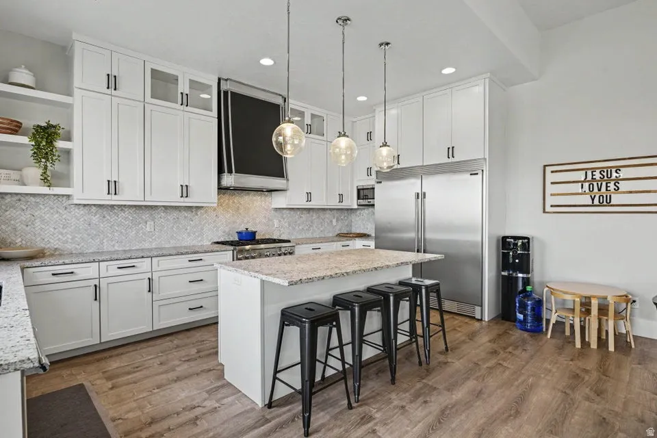 Modern kitchen featuring white cabinetry, a large kitchen island with seating, pendant lighting, stainless steel appliances, and wood-finish flooring
