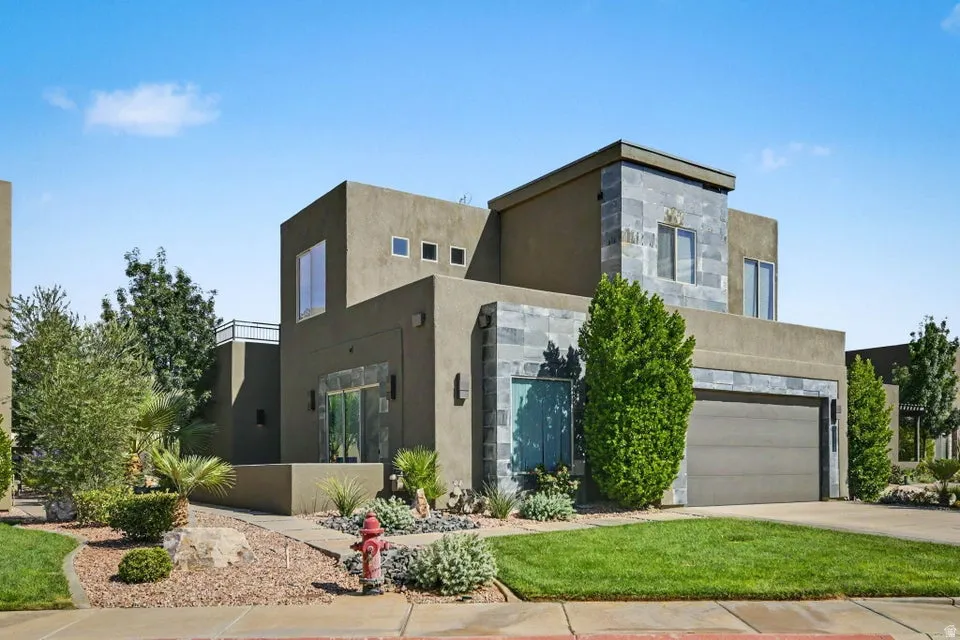 Contemporary stucco exterior with stone accents, a two-car garage, manicured lawn, and desert-style landscaping