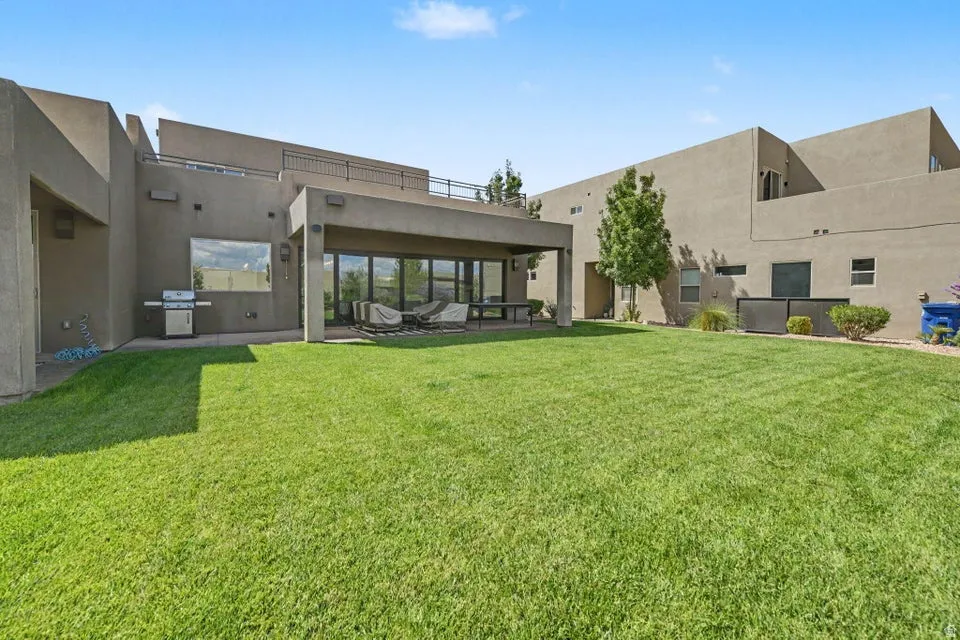 Expansive green lawn, covered patio, large sliding glass doors, upper level balcony, and mature landscaping