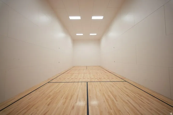 Indoor court featuring wood flooring with black and red court lines, white wall panels, and recessed ceiling lighting