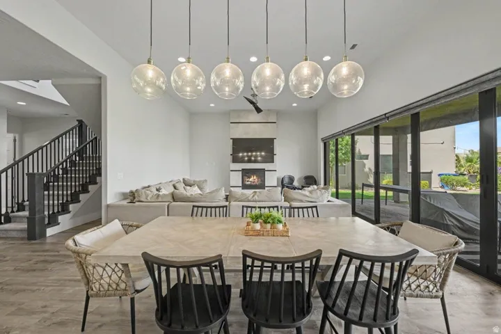 Vaulted ceiling with linear pendant lighting, fireplace with integrated media space, full-height sliding glass doors, and wood-finish flooring